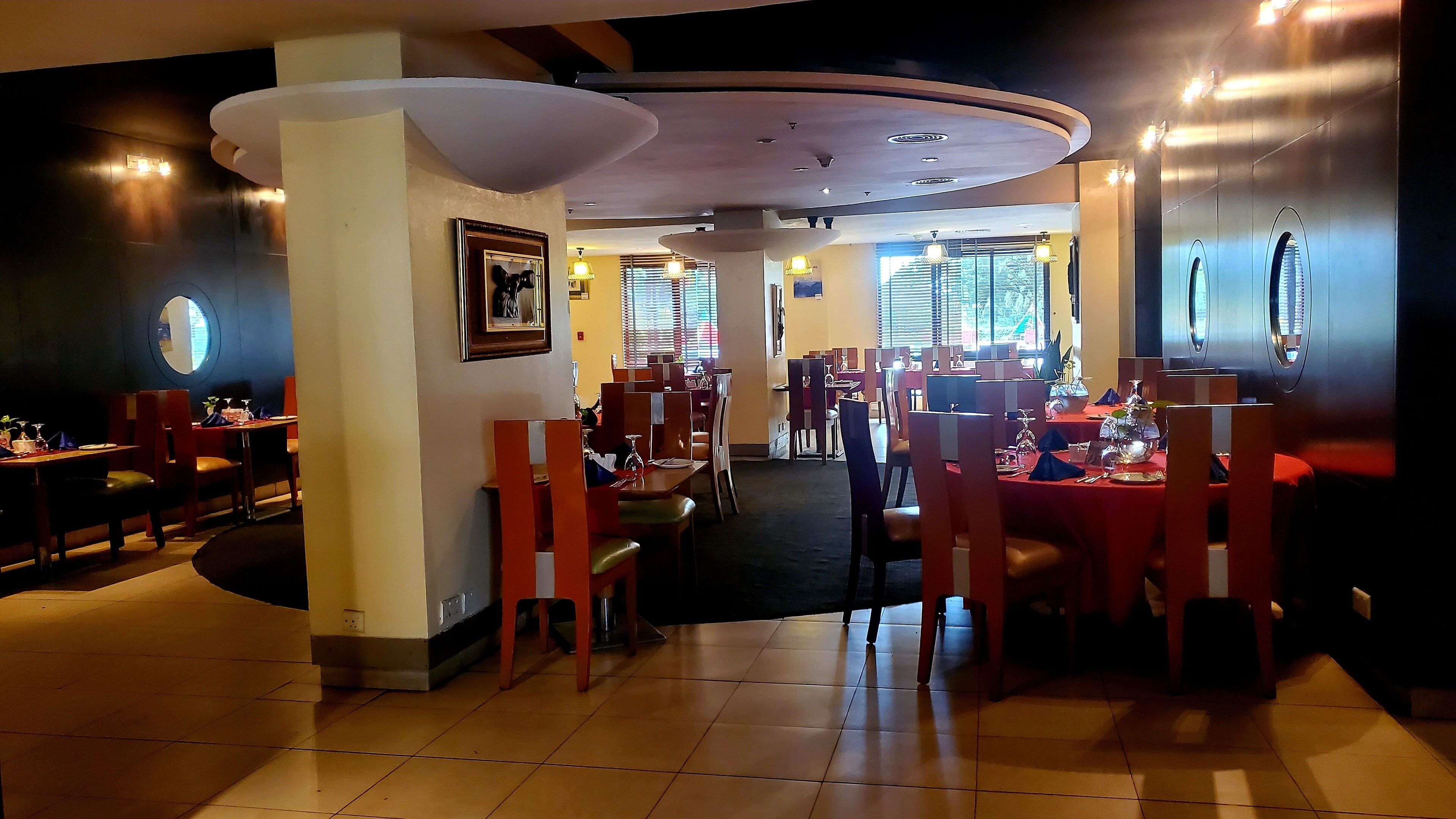 Un restaurante con varias zonas de comedor, incluyendo cabinas y mesas, con piso de baldosas e iluminación empotrada en el techo.
