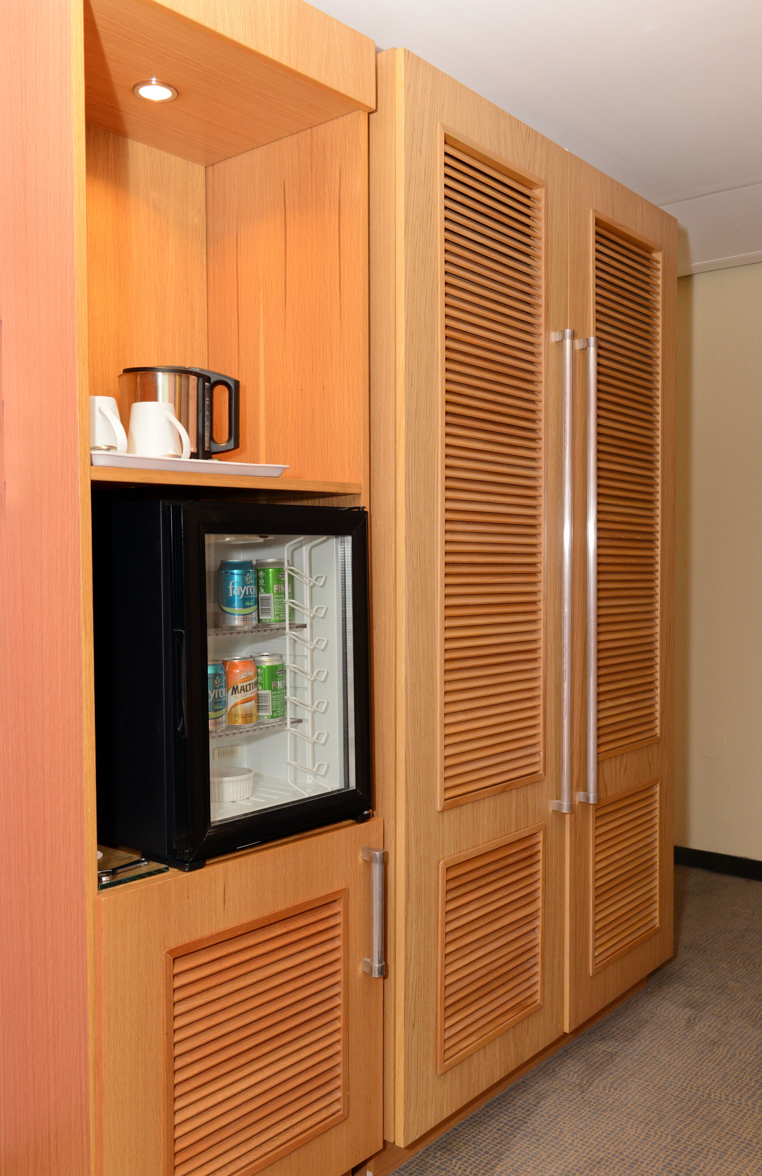 A wooden wardrobe with a built-in mini-fridge containing beverages and a microwave.