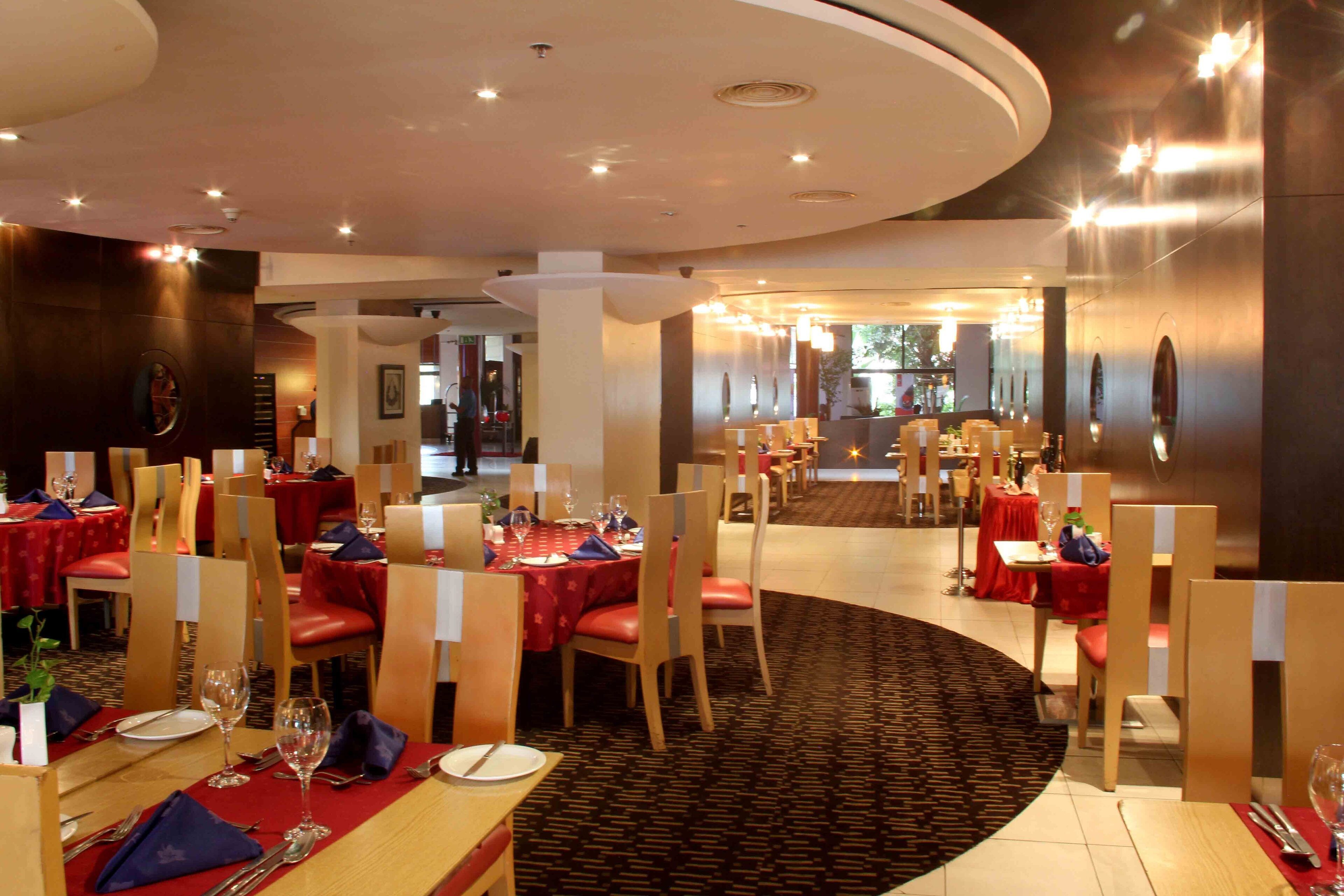 A restaurant with round tables, red tablecloths, and wooden chairs.