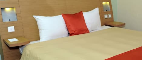 A hotel room with a wooden headboard, a bed with white and red pillows, and bedside tables with lamps.