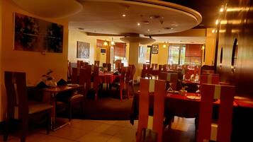 A restaurant with multiple dining tables and booths, arranged in a spacious layout with high ceilings and recessed lighting.
