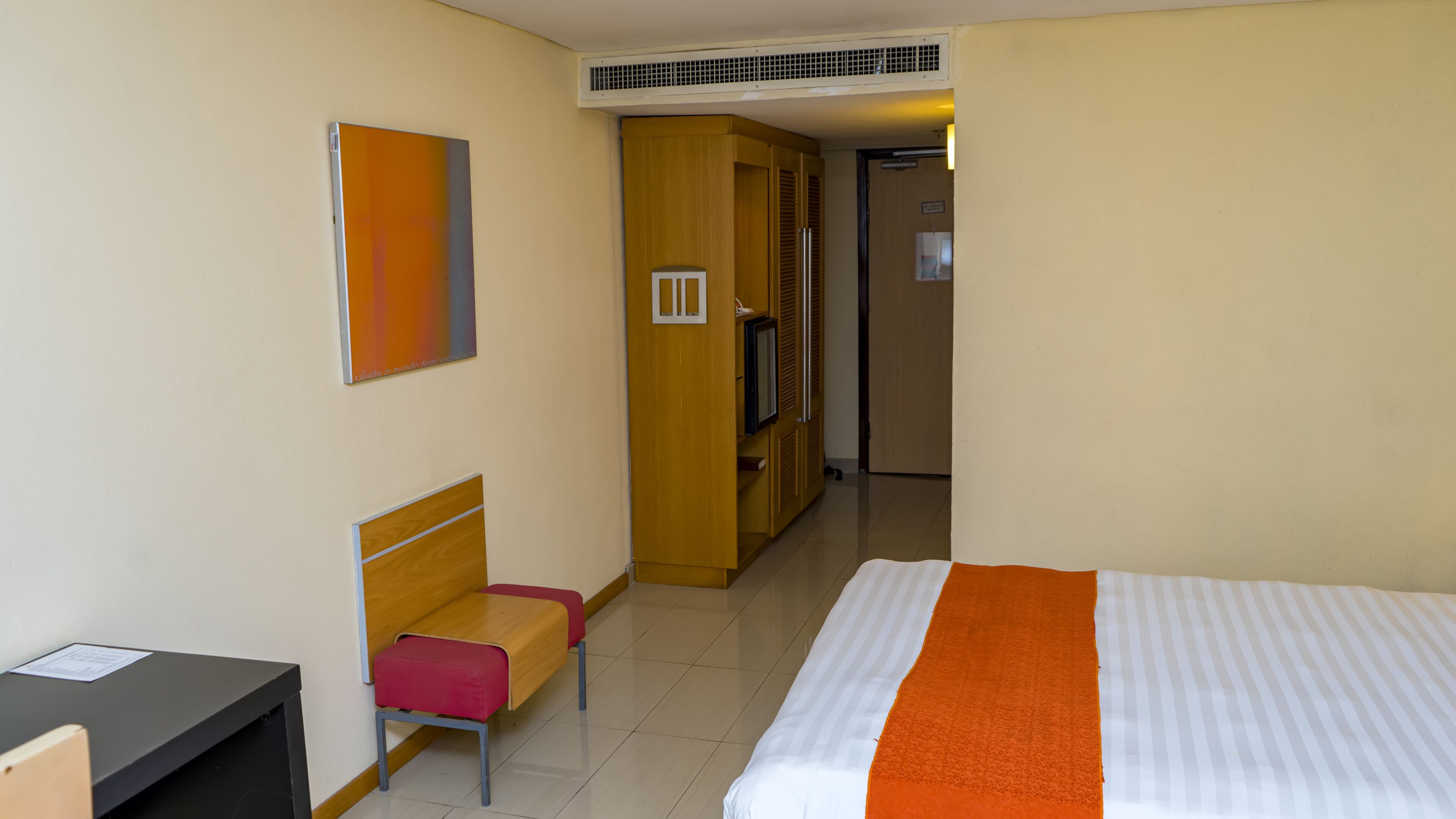 A hotel room with a bed, a desk, a chair, a wardrobe, and a television.