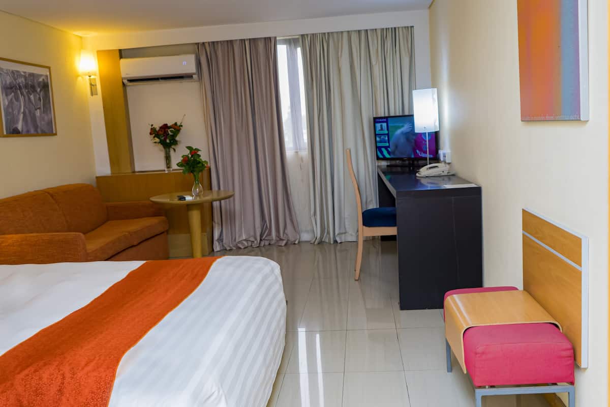 Ein Hotelzimmer mit Bett, Schreibtisch, Stuhl, einem kleinen Tisch mit einer Vase und einem Fenster mit Vorhängen.