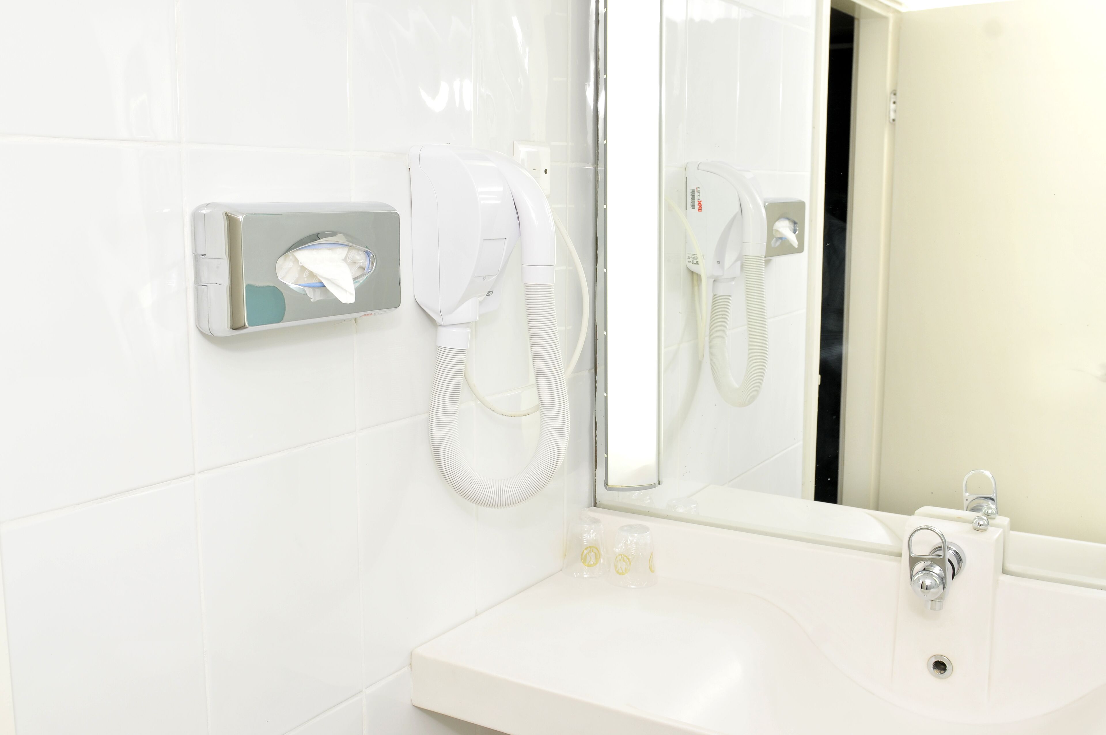 A modern bathroom with a white sink, a mirror, and a towel dispenser.