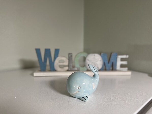 A light blue whale figurine on a white shelf with the word "WELCOME" in the background. - The White Sand Beaches are calling you (Fort Walton Beach)