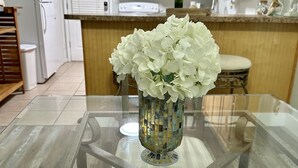 Un tavolo da pranzo con piano in vetro e un vaso di fiori bianchi al centro.