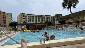 Area piscina con lettini, un bar a bordo vasca e un edificio sullo sfondo.