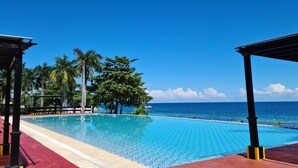 Une piscine avec vue sur l’océan, entourée de palmiers et dotée d’un espace abrité.