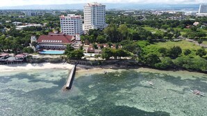 Vue aérienne d’un hôtel situé sur la côte, avec une piscine, des villas en bord de mer et une jetée qui s’avance dans l’océan.