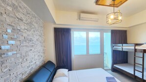 Une chambre d’hôtel avec un lit, un banc, un mur au motif de briques, une fenêtre et un luminaire au plafond.