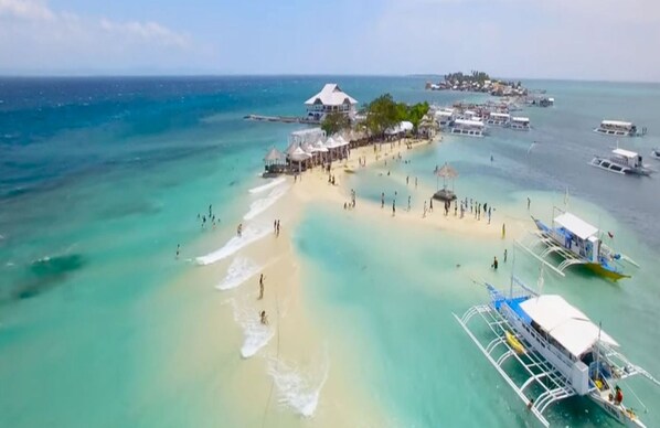 An aerial view of a beach with clear turquoise waters, a sandy shore, and several boats. - New Huge 2 BR Oceanfront - condo (100sqm) (Lapu-Lapu City)