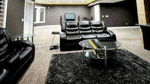 A modern living room with a black leather sofa, a glass coffee table, and a flat-screen TV mounted on the wall. - Beautiful 1 bedroom Basement in an Acreage (Delacour)