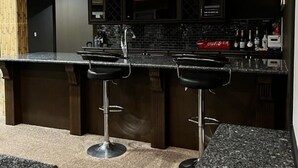 A modern kitchen with dark cabinetry, a granite countertop, and two bar stools. - Beautiful 1 bedroom Basement in an Acreage (Delacour)