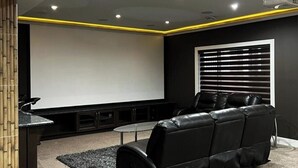 A home theater room with a black leather sofa, a large screen, and a projector. - Beautiful 1 bedroom Basement in an Acreage (Delacour)