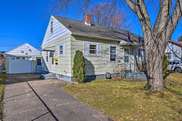 A two-story house with a garage, a tree in front, and a clear blue sky.