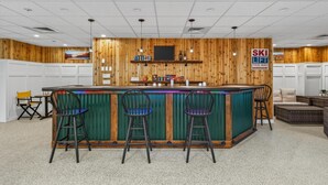 A bar area with a wooden wall, three stools, and a sign indicating a ski lift direction. - Pinnacle B18 (Killington)