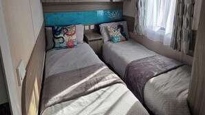 Een compact slaapkamerinrichting in een camper, met twee bedden, een inbouwplankje en een raam met behang.