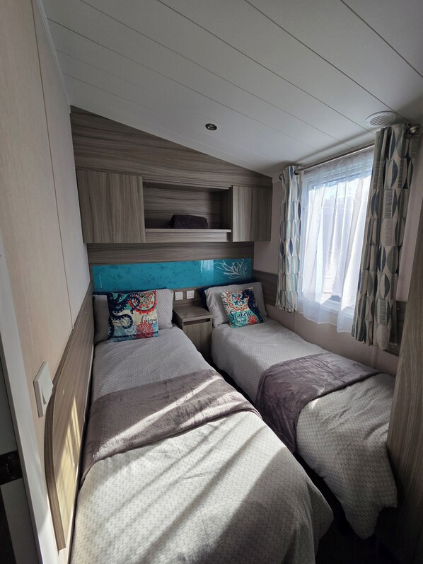 Een compact slaapkamerinrichting in een camper, met twee bedden, een inbouwplankje en een raam met behang.