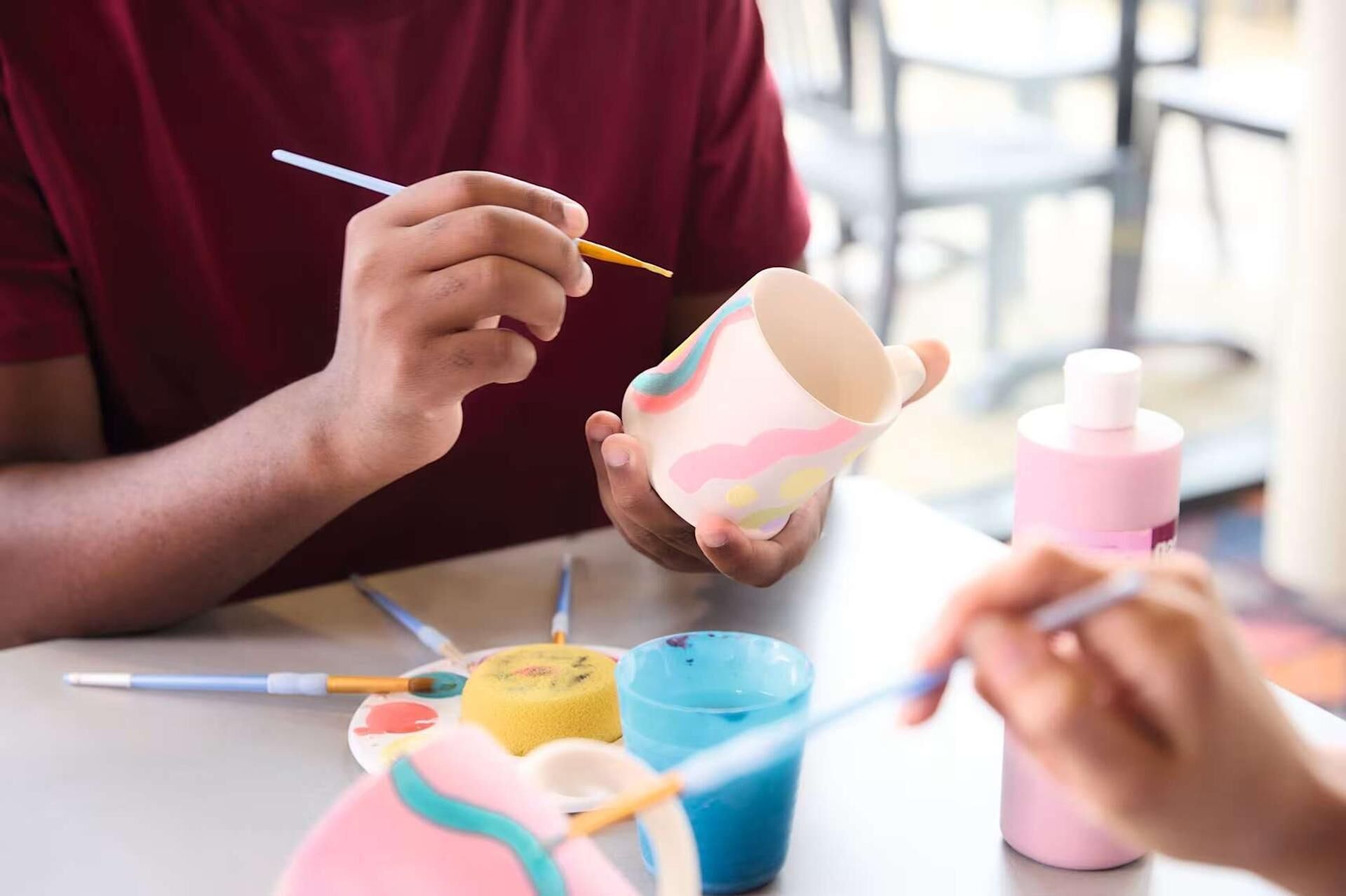 Une personne est en train de peindre une tasse en céramique avec des motifs colorés.