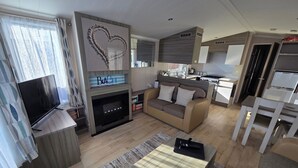 Een moderne woonkamer met een flatscreen televisie, een bank, een salontafel en een keukenhoek met een fornuis en een koelkast.