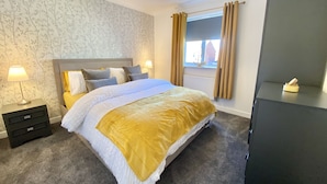 Une chambre à coucher bien rangée, avec un grand lit, des lampes de chevet, une commode et une fenêtre avec des rideaux.