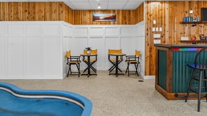 A pool area with a wooden wall, a small table with chairs, and a bar counter with snacks. - Pinnacle A11 (Killington)