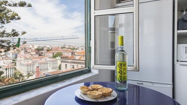 A table with a plate of pastries and a bottle of liquor by a window overlooking a cityscape. - The Castle Life in Lisboa Ciudad (Lisbon)