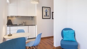 A compact kitchen with white cabinets, a stove, and a sink. There is a dining area with a white table and blue chairs. A framed artwork is on the wall. - The Castle Life in Lisboa Ciudad (Lisbon)
