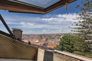 Blick aus einem Fenster auf eine Stadtlandschaft mit roten Dächern und einem klaren Himmel.