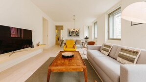 A modern living room with a wooden coffee table, a sofa, and a yellow armchair. There is a dining area in the background with a table and chairs. - Lady Madonna in Lisboa Ciudad (Lisbon)