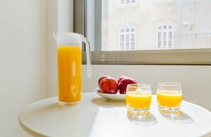A table with a pitcher of orange juice, two glasses of orange juice, and a bowl of red apples.