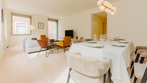 A modern dining area with a large table set for a meal, surrounded by wicker chairs and a sofa. - Lady Madonna in Lisboa Ciudad (Lisbon)