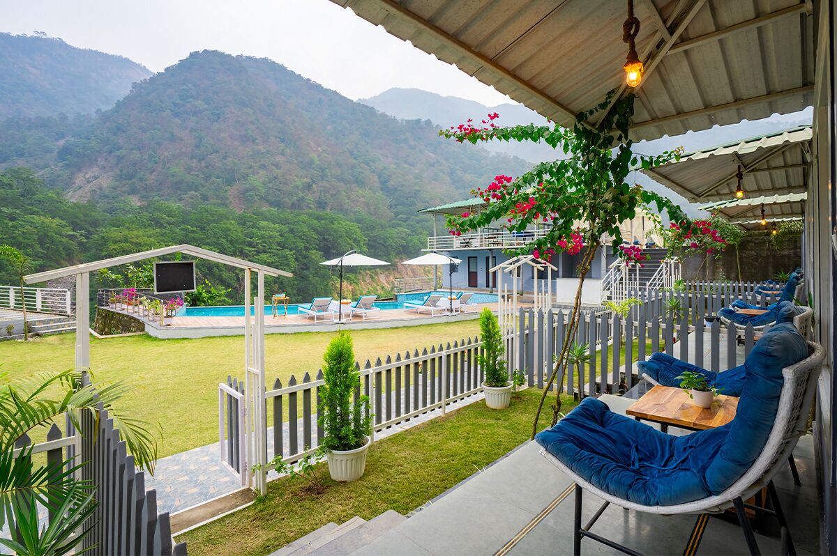 A covered outdoor seating area with a pool, white picket fence, and a view of mountains.