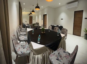 Un salón de conferencias con una mesa redonda, sillas estampadas con motivos florales y botellas de agua sobre la mesa.