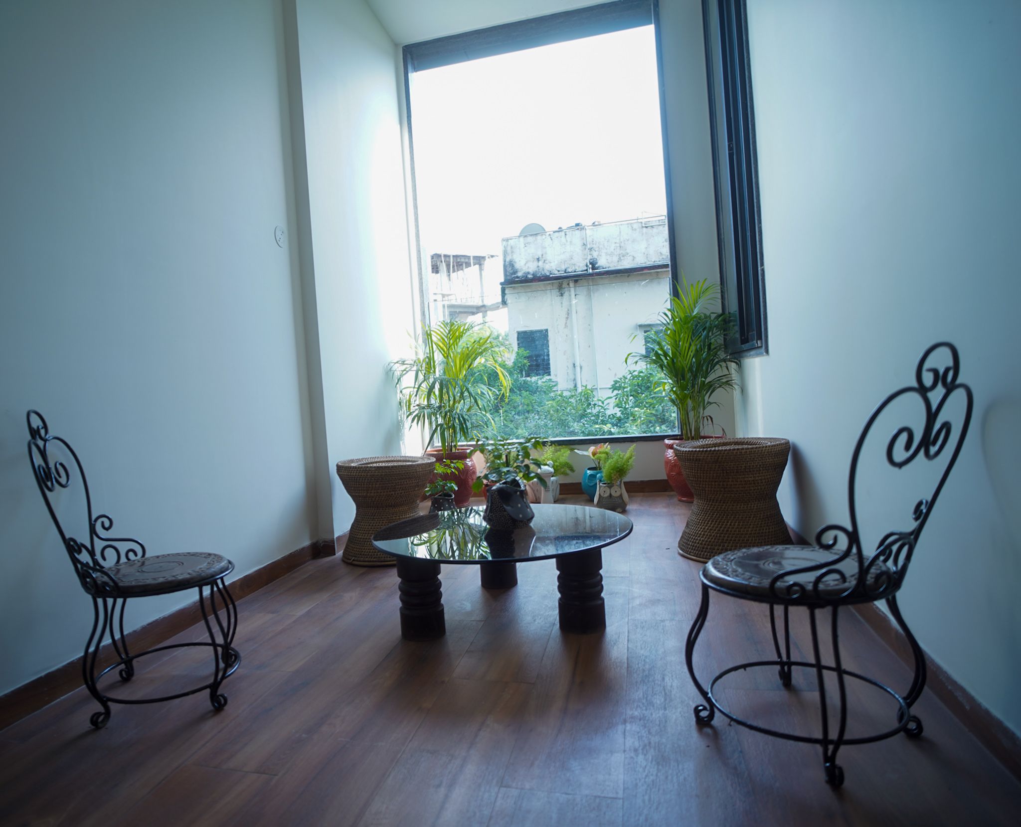 A balcony with a round table and two chairs, potted plants, and a view of buildings.
