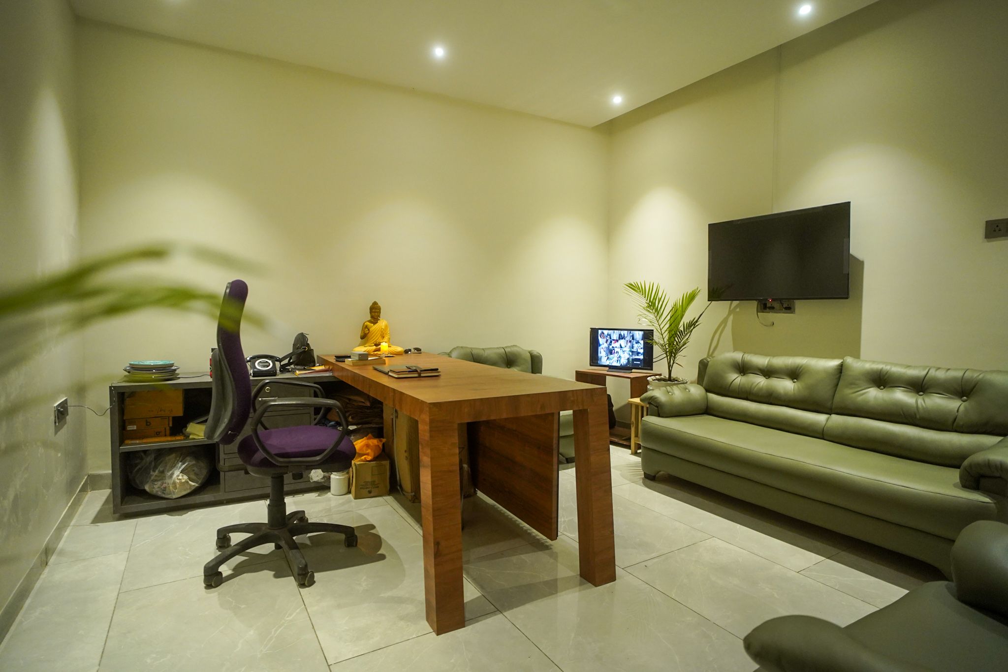 A modern living room with a wooden table, a green sofa, a television, and a Buddha statue.
