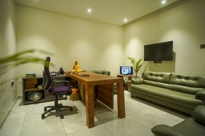 A modern living room with a wooden table, a green sofa, a television, and a Buddha statue. - Hotel Lunar Stays (Bhopal)