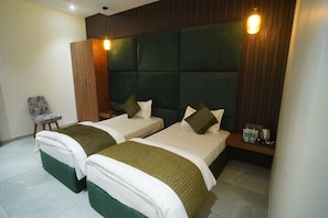 Una habitación de hotel con dos camas, un armario de madera, una silla y una mesita de noche con botellas.