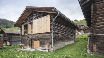 A rustic log cabin with a wooden door, a small porch, and a window.