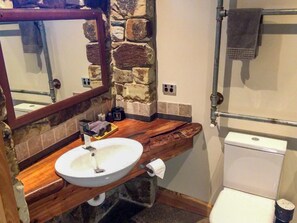 Un baño con pared de piedra, tocador de madera, lavamanos blanco y un inodoro.