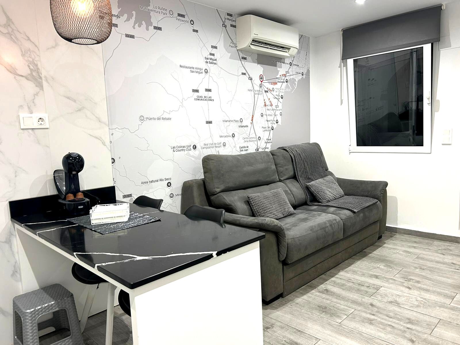 Un salon moderne avec un canapé gris, une machine à café et une carte accrochée au mur.