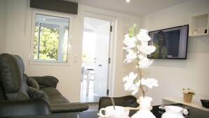 A modern living room with a sofa, a coffee table, and a TV mounted on the wall. There is a door leading to an outdoor area. - Relax & Comfort in Lago Jardín • Garden Bungalow • Community Pool(35) (LOS BALCONES)
