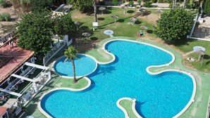 A large, uniquely shaped pool with multiple sections, surrounded by a well-maintained lawn and shaded by umbrellas. - Relax & Comfort in Lago Jardín • Garden Bungalow • Community Pool(35) (LOS BALCONES)