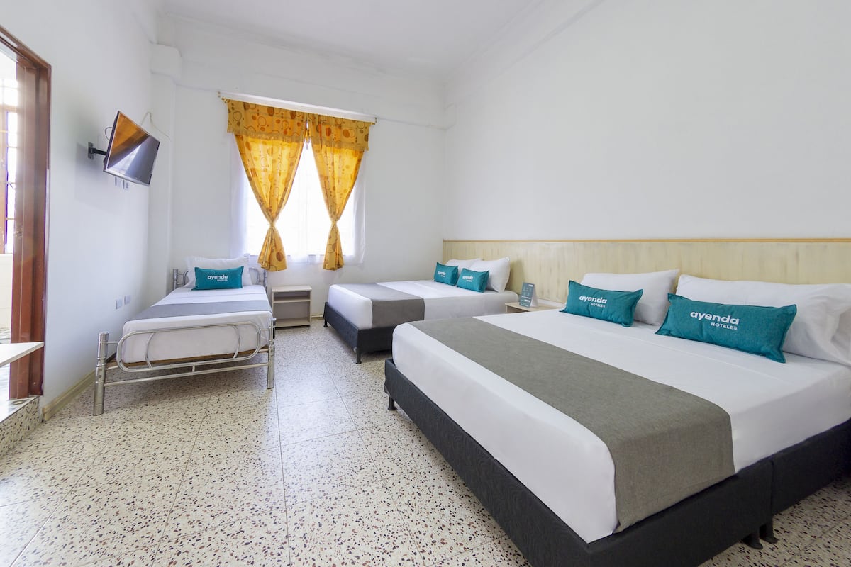 Ein Hotelzimmer mit zwei Einzelbetten und einem größeren Bett, jeweils mit weißer Bettwäsche und türkisfarbenen Kissen.