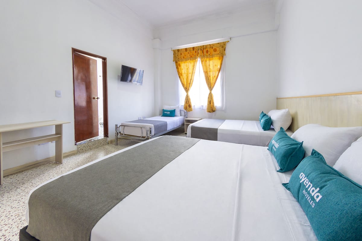 Ein Hotelzimmer mit zwei Einzelbetten, einem Schreibtisch, einem Stuhl, einem Fernseher und einem Fenster mit Vorhängen.
