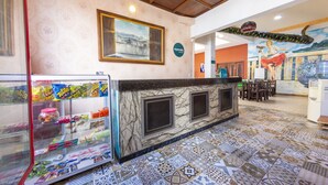 Un vestíbulo de hotel con un mostrador de recepción de mármol, una vitrina con aperitivos y un mural en la pared.