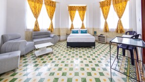 Habitación de hotel con una cama, dos sofás grises, una mesita pequeña y una mesa de cristal con una silla.