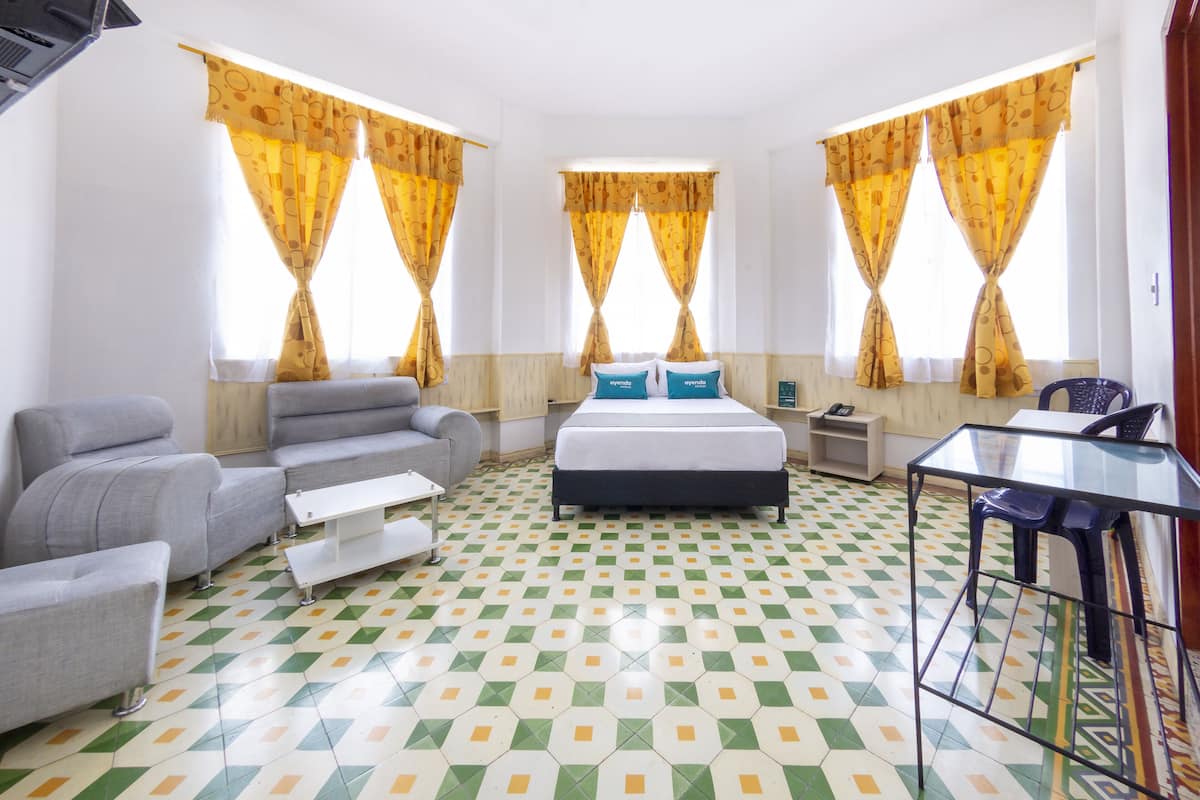 Ein Hotelzimmer mit einem Bett, zwei grauen Sofas, einem kleinen Tisch und einem Glastisch mit einem Stuhl.