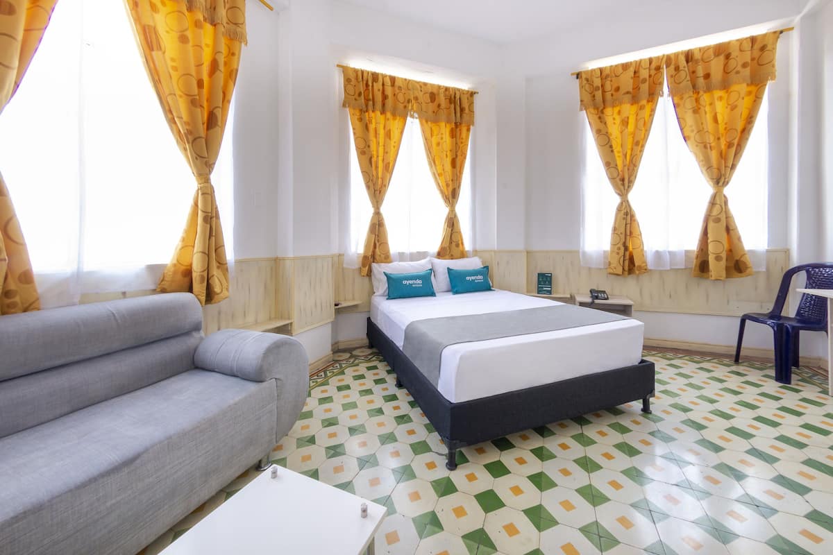 Ein Hotelzimmer mit einem Bett, einer Couch, einem Sessel und fußbodenhohen, gemusterten Fliesen.