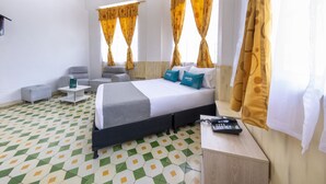 Una habitación de hotel con una cama, dos sillones, una mesita y una mesita de noche con un teléfono.